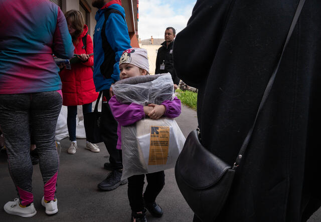 A young girls stands in a crowd, holding a blanket distributed by the IRC.